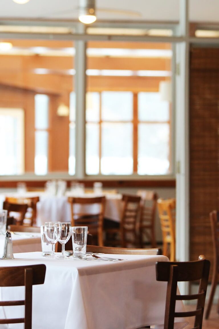 A serene restaurant interior with wooden chairs and tables set with glasses, ready for dining.